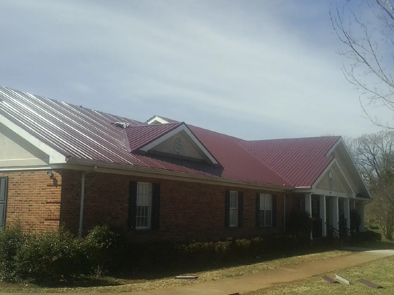 Red metal roof with gabled entries on a long brick building, from a Hail Damage Roof Repair job in Waleska