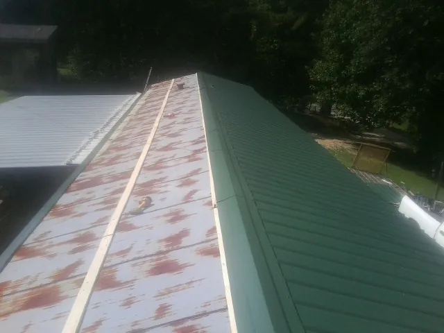 Old rusted panels beside newly installed green metal roofing — Wind Damage Roof Repair by Roofing Brothers in Waleska
