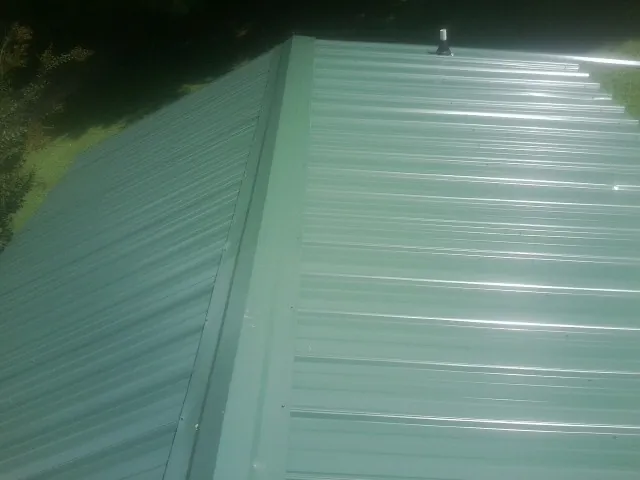 New green metal panels meeting at the ridge of a roof — Flat Roof Repair work by our crew in Waleska