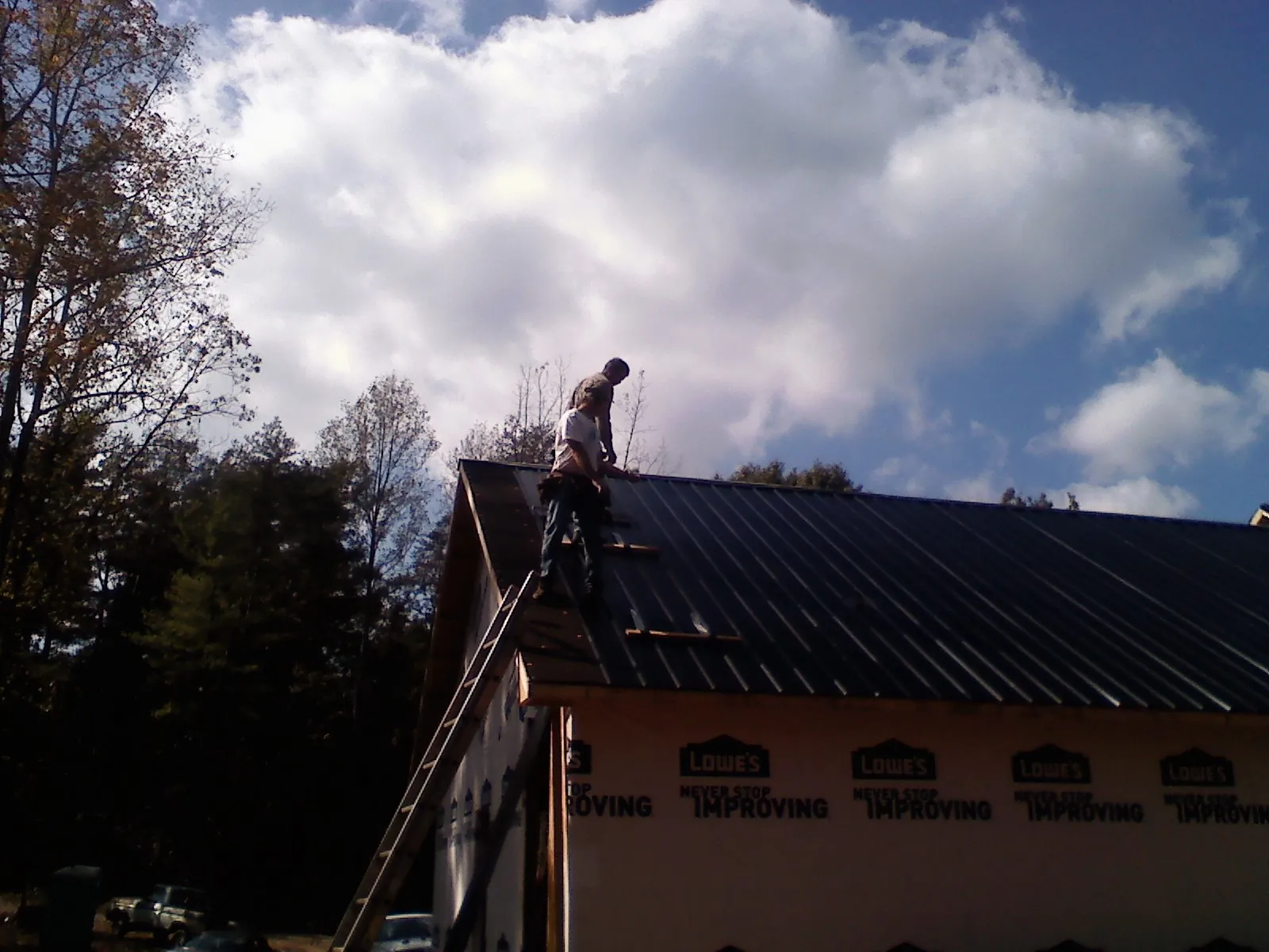 Roofer fastening dark metal panels high against a cloudy sky, from a Roof Inspection job in Waleska