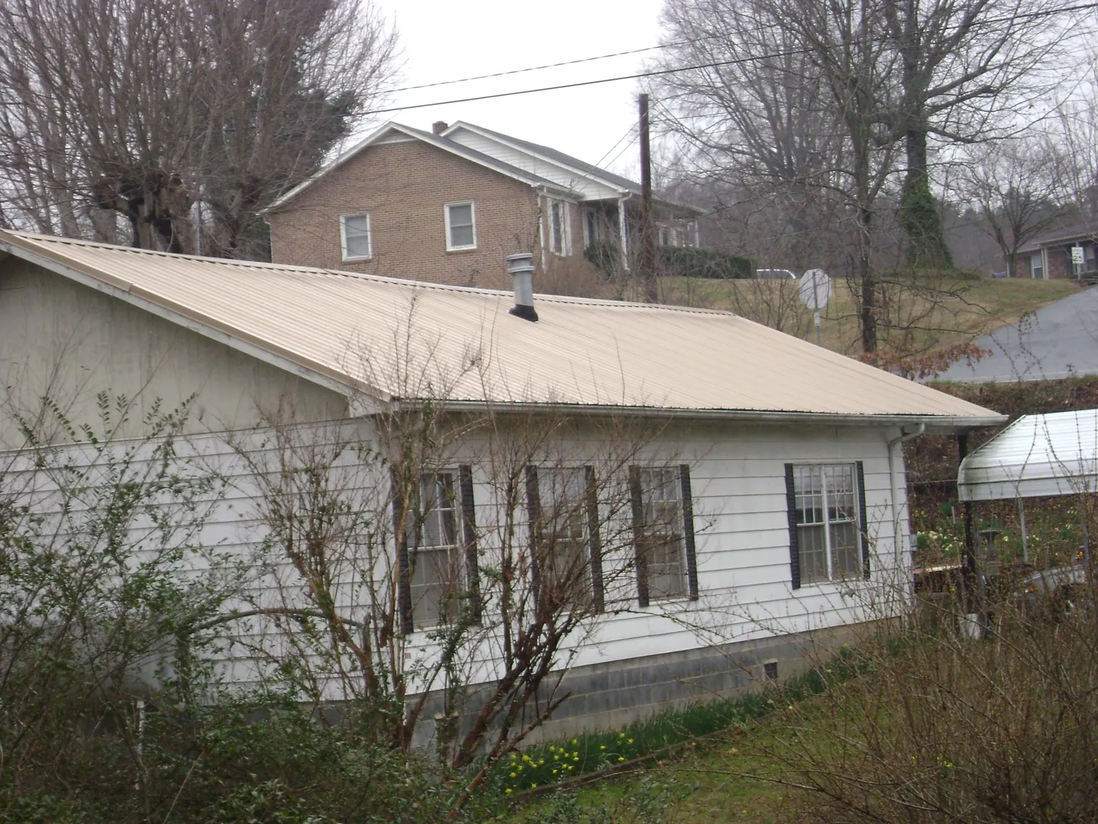 Tan metal roof on a white sided house set into a hillside — Commercial Roofing by Roofing Brothers in Waleska
